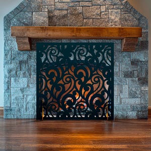 May include: A black metal fireplace screen with a decorative, ornate design. The screen is in front of a stone fireplace with a wood mantel.