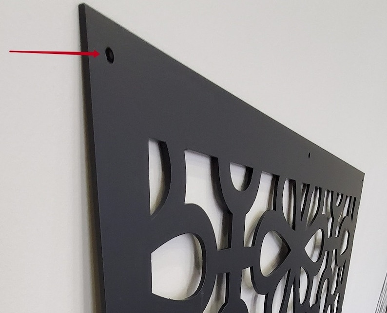 May include: A black decorative wall panel with a geometric cut-out design. The panel is mounted on a white wall and has a matte finish. The panel has a series of holes for mounting.