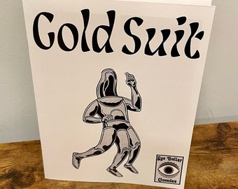 May include: A white comic book with the title "Cold Suit" in black lettering. The cover features a black and white illustration of a robot-like figure in a suit. The bottom right corner has a logo that says "Eye Baller Comics".