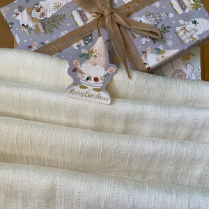 Puede incluir: Una bolsa de regalo blanca con una caja de regalo gris y blanca con una cinta marr&oacute;n y una etiqueta de regalo de gnomo que dice "Feliz Navidad".