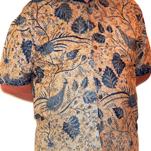 Peut inclure: Une chemise à manches courtes à boutons avec un fond beige et un motif floral bleu. Le motif présente des feuilles, des vignes et des oiseaux.