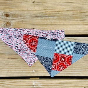 May include: Two triangular pet bandanas. One features a white background with small red and blue stars. The other is a patchwork design with red and navy blue paisley patterns combined with a light blue and white gingham check fabric pattern.