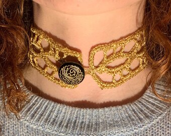 May include: A gold crocheted choker necklace with a black button featuring a swirl design.