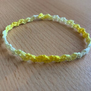 May include: A yellow and white crocheted bracelet with a graduated color pattern.