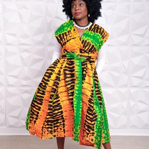 May include: A sleeveless wrap dress featuring a vibrant pattern of orange, yellow, and green with black abstract markings. The dress has a V-neckline, a cinched waist with a tie belt, and a full, pleated skirt that falls below the knee.