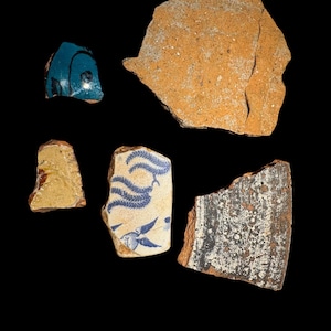 May include: Collection of pottery shards in various shapes and sizes. The fragments display a range of colors, including blue, yellow, and brown. Some pieces feature decorative patterns, while others are plain.