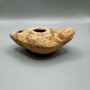 Puede incluir: Una taza de cerámica blanca con asa negra y el texto "But First, Coffee" en negrita negra. La taza se encuentra sobre un fondo borroso, sugiriendo un ambiente acogedor.