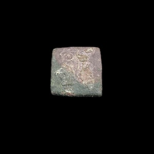 Può includere: Un piccolo oggetto di forma quadrata con una superficie ruvida e usurata. Il pezzo presenta un mix di toni marrone rossastro spento e grigio-verde scuro, con macchie irregolari e una finitura grezza su tutta la sua superficie.