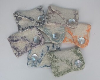 May include: A collection of seven small, rectangular felt pouches in off-white, each featuring a unique marbled pattern in shades of blue, purple, green, or orange. Each pouch is secured with a single, round, iridescent mother-of-pearl button.