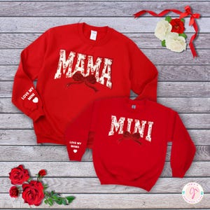 May include: Red sweatshirts with white lettering that says "Mama" and "Mini" with a red bow design. The sleeves have white lettering that says "Love my Mini" and "Love my Mama" with a small red heart.