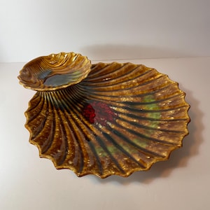 May include: A decorative, ceramic serving dish in the shape of a seashell. The dish is a warm brown color with darker brown and green accents. A smaller, matching dish sits atop the larger one. The dish has a ridged texture.