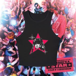 May include: Black tank top featuring a pink star graphic with a portrait of a person. The tank top is set against a background of a crowd of people. The text on the bottom right says "Everyone's a Star, Your #1 Obsession."