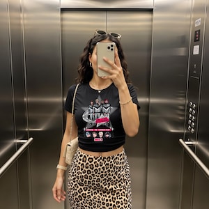 Könnte beinhalten: Schwarzes Crop-Top mit einem grafischen Design, das eine Gruppe von Figuren vor einem Stern und dem Text "CHOOSE YOUR CHARACTER" zeigt. Die Person trägt einen Leopardenrock und eine Sonnenbrille.