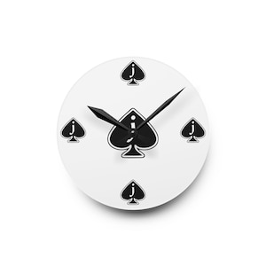 May include: White round wall clock with black spade suit symbols and black clock hands. The clock face features a large spade in the center and smaller spades at the 12, 3, 6, and 9 o'clock positions. The clock hands are black.