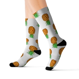 May include: A pair of white socks with a pineapple pattern. The socks are shown on a model's legs.
