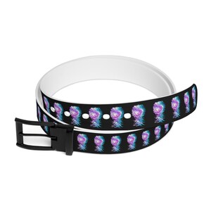 Puede incluir: Un cinturón reversible blanco y negro con un estampado de piña colorido. El cinturón tiene una hebilla negra y está hecho de un material duradero.