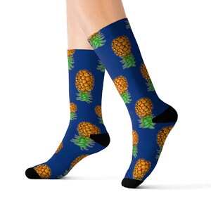 Puede incluir: Un par de calcetines azules con un patrón de piña. Las piñas son amarillas con hojas verdes y están dispersas por los calcetines.