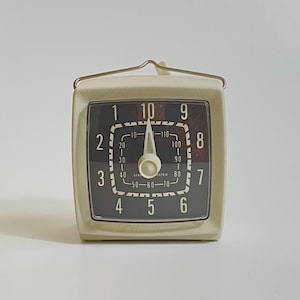 May include: A beige kitchen timer with a black face and white numbers. The timer has a white knob and a metal loop on the top.