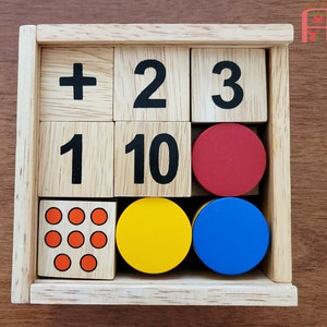 May include: Wooden box with a set of colorful blocks. The blocks have numbers and symbols on them, including the numbers 1, 2, 3, 10, and a plus sign. There are also red, blue, and yellow circles.