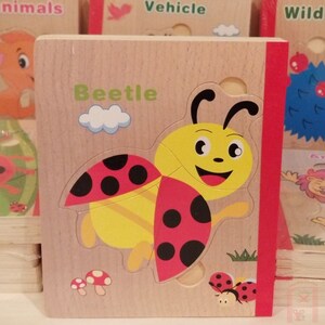 May include: A wooden puzzle book with a colorful illustration of a ladybug on the cover. The book has the word "Beetle" printed on the cover.