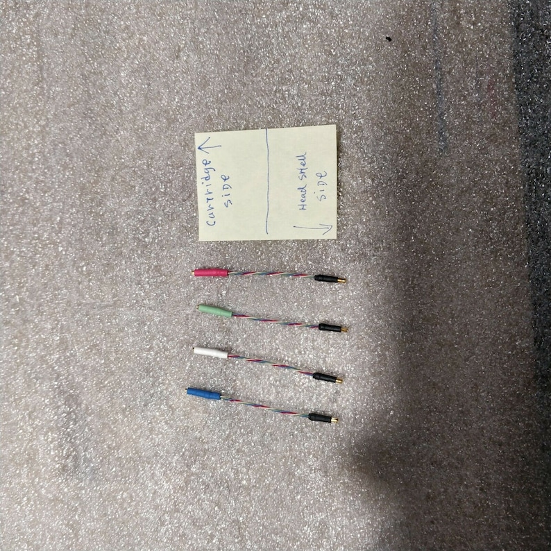 May include: Four sets of audio cartridge wires with colored ends: pink, green, white, and blue. Each wire set has a black connector on one end and a gold connector on the other. A handwritten note indicates "Cartridge side" and "Head shell side."
