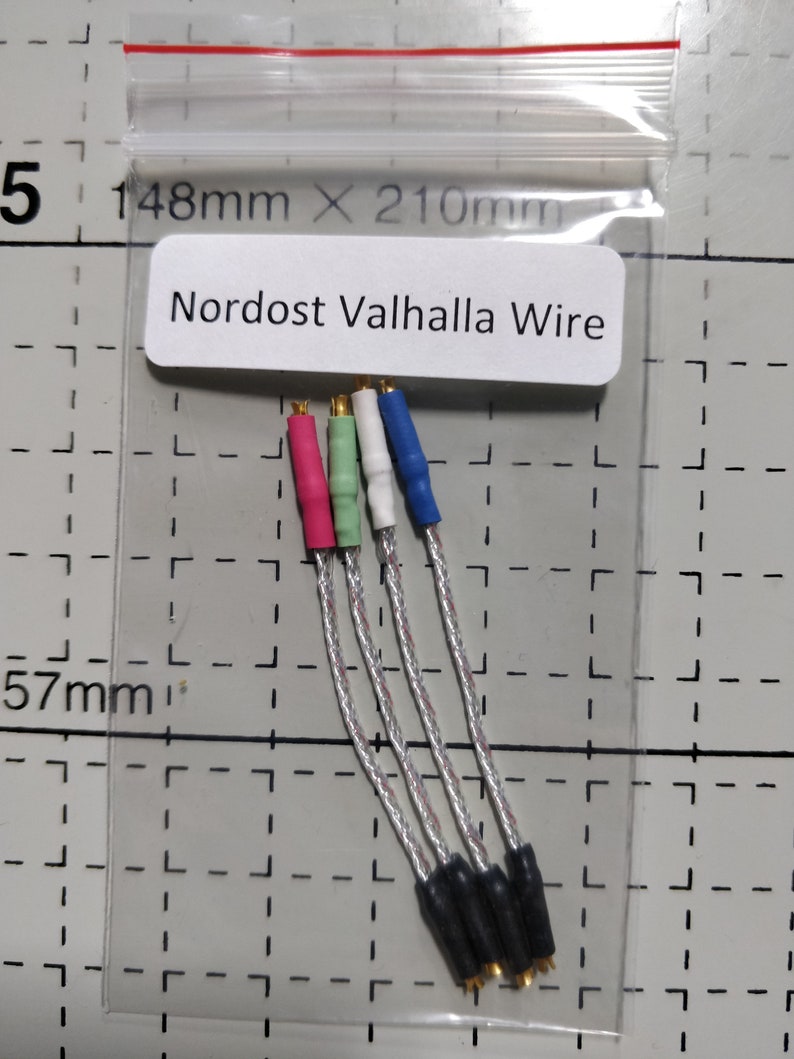 May include: A clear plastic bag containing four Nordost Valhalla wires. Each wire has a different colored connector: pink, green, white, and blue. The wires are silver and black. The text "Nordost Valhalla Wire" is printed on a white label.