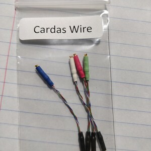May include: A clear plastic bag containing several audio cables. The cables have colored connectors in blue, white, red, and green. The label on the bag reads "Cardas Wire". The wires are multi-colored and twisted.