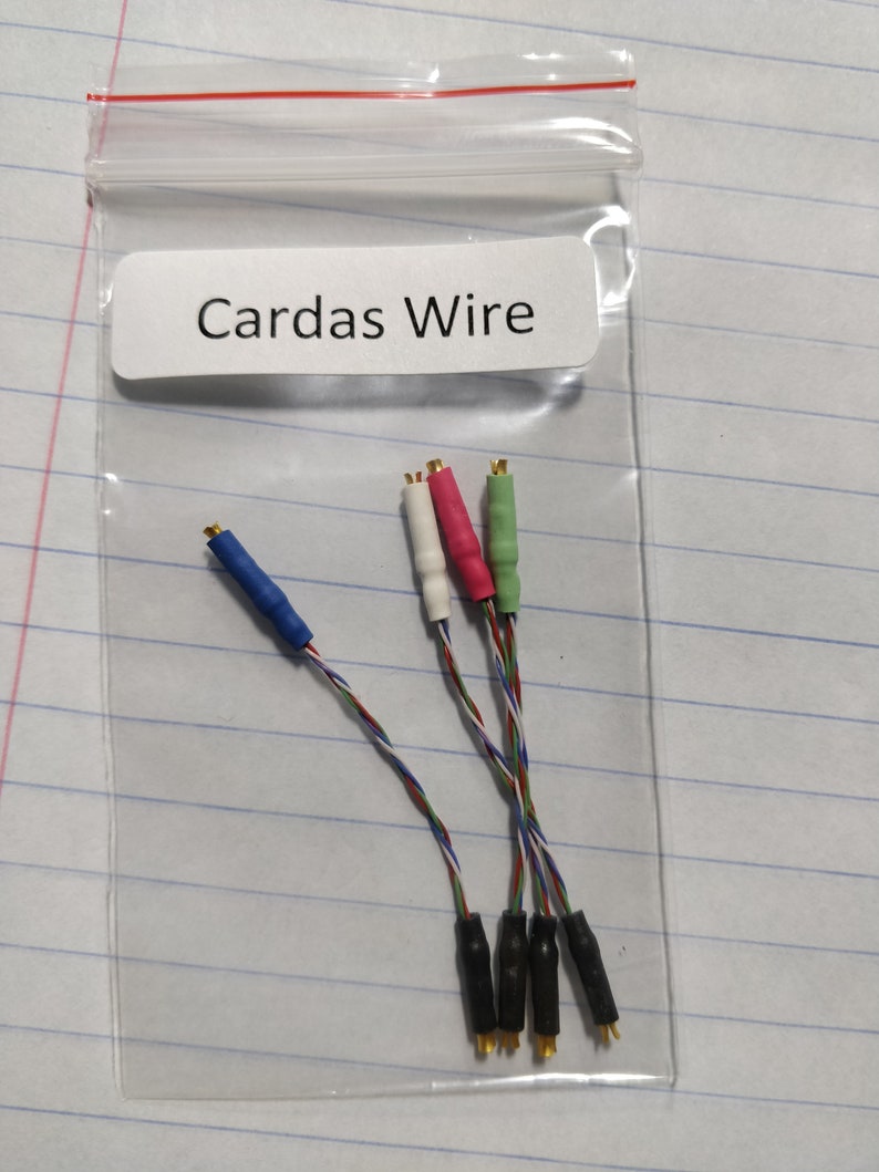 May include: A clear plastic bag containing several audio cables. The cables have colored connectors in blue, white, red, and green. The label on the bag reads "Cardas Wire". The wires are multi-colored and twisted.