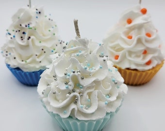 May include: Three cupcake-shaped candles with white frosting and colorful sprinkles. The candles have blue, yellow, and teal bases. Each candle has a wick extending from the top, resembling a real cupcake.