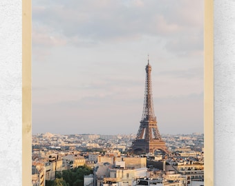 May include: A framed print of the Eiffel Tower in Paris, France, under a cloudy sky. The image shows the tower rising above a cityscape of buildings and rooftops, presented within a light-coloured wooden frame.