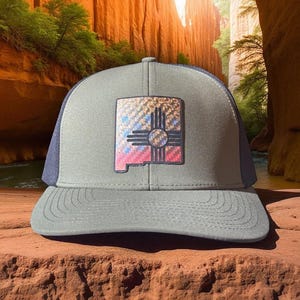 Può includere: Cappellino da camionista grigio e blu navy con il simbolo Zia del New Mexico sul davanti. La toppa ha un design colorato con tonalità rosse, blu, gialle e marroni. Il cappellino ha una visiera curva e un retro in rete.