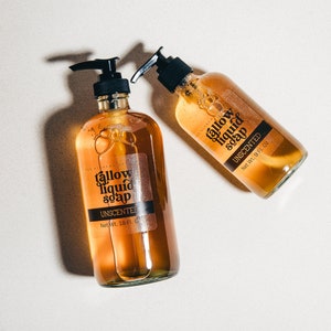 May include: Two amber glass bottles of unscented tallow liquid soap with black pump tops. The bottles are labelled "tallow liquid soap" and "UNSCENTED". The bottle on the left is 18 fl oz and the bottle on the right is 9 fl oz.