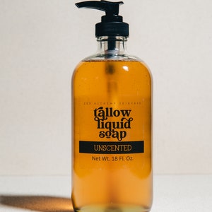 May include: A clear glass bottle with a black pump dispenser filled with a golden liquid. The bottle has a black label with the text "EGG ALCHEMY SKINCARE tallow liquid soap UNSENTED Net Wt. 18 Fl. Oz."