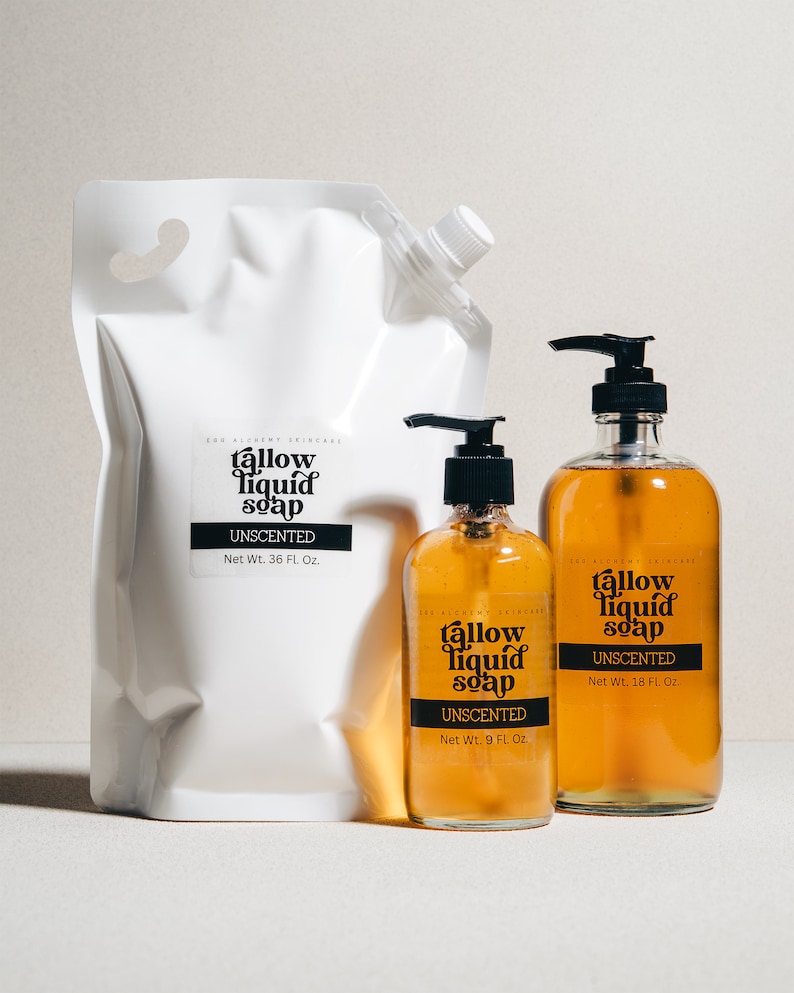 May include: Three bottles of unscented tallow liquid soap in different sizes. The bottles are amber glass with black pump tops. The labels are black with white text and say "tallow liquid soap" and "unscented". The largest bottle is a white plastic pouch with a spout.