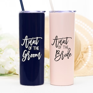 May include: Two stainless steel tumblers with lids and straws. The tumbler on the left is navy blue with white text that says "Aunt of the Groom". The tumbler on the right is pink with black text that says "Aunt of the Bride".