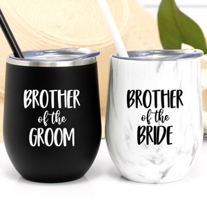 May include: Two stainless steel wine tumblers with lids and straws. The tumbler on the left is black with white text that reads "Brother of the Groom". The tumbler on the right is white with black marble pattern and black text that reads "Brother of the Bride".