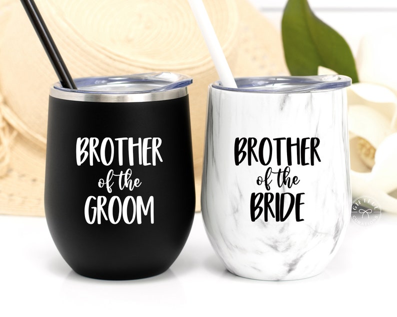 May include: Two stainless steel wine tumblers with lids and straws. The tumbler on the left is black with white text that reads "Brother of the Groom". The tumbler on the right is white with black marble pattern and black text that reads "Brother of the Bride".