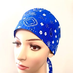 Puede incluir: Un gorro de quirófano azul con un patrón paisley blanco. El gorro tiene un lazo en la parte posterior.