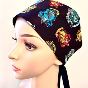 Può includere: Cappello chirurgico nero con un motivo ripetuto degli stemmi delle case di Hogwarts. Gli stemmi sono nei loro colori tradizionali: Grifondoro (rosso e oro), Tassorosso (giallo e nero), Corvonero (blu e bronzo) e Serpeverde (verde e argento).