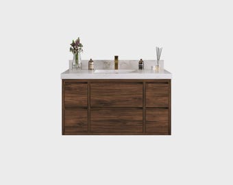 May include: A modern bathroom vanity with a white marble countertop and a dark wood cabinet. The vanity has a gold faucet, a built-in sink, and several drawers. Decorative items include a vase of flowers and bottles.