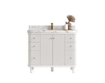 May include: A white bathroom vanity with a marble countertop and gold fixtures. The vanity has a ribbed design on the doors and drawers, with gold hardware. Decorative items sit on the countertop, including a vase and a bottle.