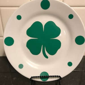 May include: White ceramic plate with a green four-leaf clover design and green polka dots around the edge.