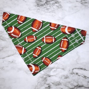 May include: Green and white fabric dog bandana with a football field pattern and brown footballs.