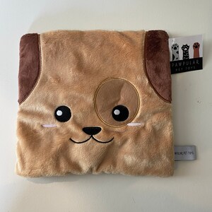 May include: A brown plush dog-shaped pillow with a brown nose, black eyes, and a brown spot on its head. The pillow has a white tag attached to it that says "Pawpular Pet Toys".