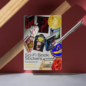 May include: A collection of Sci-Fi Book Stickers featuring various book covers and graphics. The stickers are exclusive to Magic City Memories Co. A silver pen rests on the stickers, with a red background and wooden accents.