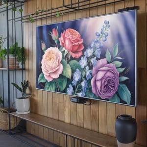 Può includere: Un'opera d'arte incorniciata con una composizione floreale di rose rosa, rosse e viola con accenti blu. L'opera è montata su una parete di legno, con una mensola in metallo nero e varie piante in vaso sullo sfondo.