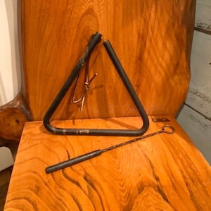 May include: A black metal triangle with a wooden mallet on a wooden surface. The triangle is a musical instrument.