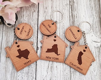 May include: Four wooden house-shaped keychains with state outlines and names. The keychains are "Jeremy & Sarah, Texas", "The Kims Family, New York", "Danielle, California", and a fourth keychain with a heart.