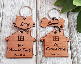 May include: Two wooden house-shaped keychains with the text "The Barnard Family" and the dates "Mar. 2022" and "Oct. 2022".  A cat-shaped keychain with the name "Lucy" and a bone-shaped keychain with the name "Cloud" are attached to the house keychains.