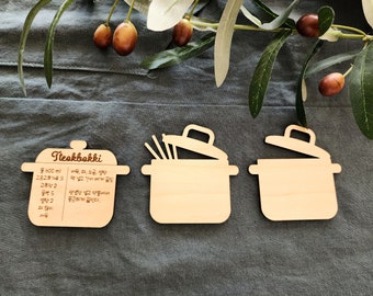 May include: Three wooden pot-shaped recipe cards. One card has a recipe for Tteokbokki with ingredients listed in Korean. The other two cards are blank.